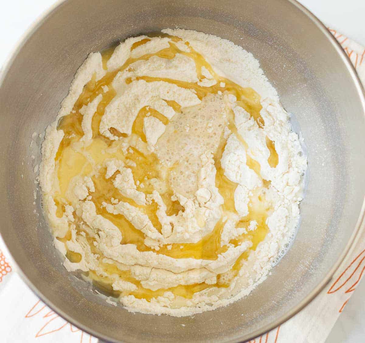 Flour, olive oil, and yeast mixture in a stand mixer bowl.