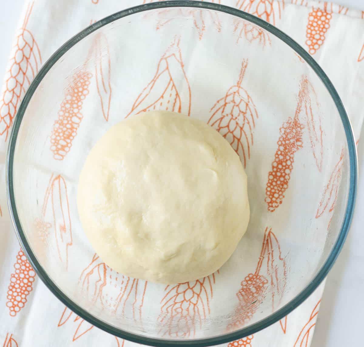 Bread dough in a glass bowl on a printed kitchen towel.