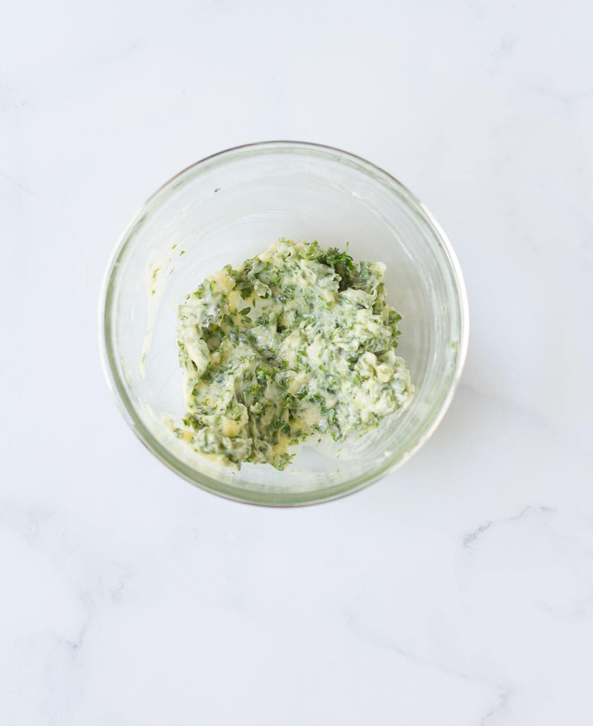 A mixture of butter, garlic, and parsley in a small bowl.