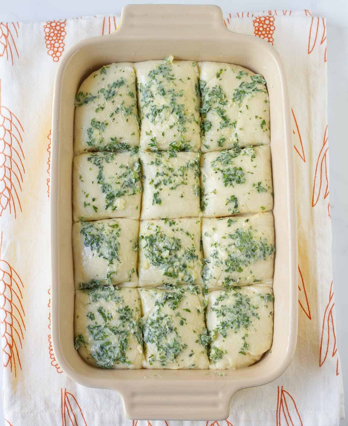 Bread dough brushed with garlic herb butter in a baking dish.