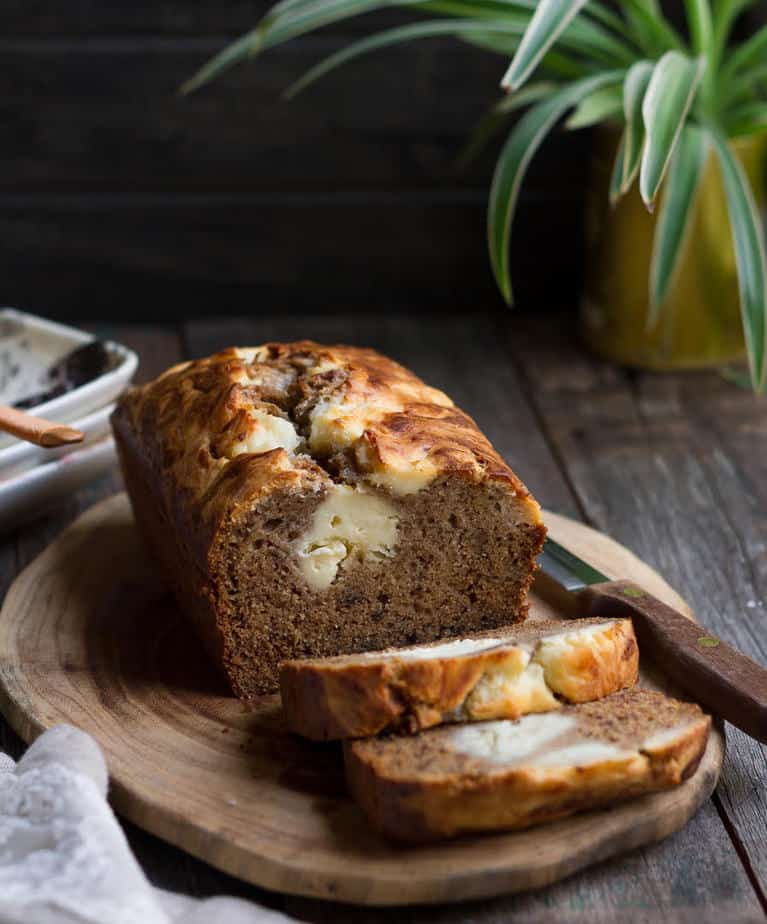 Sliced cream cheese swirl banana bread on a wooden chopping board with a knife.