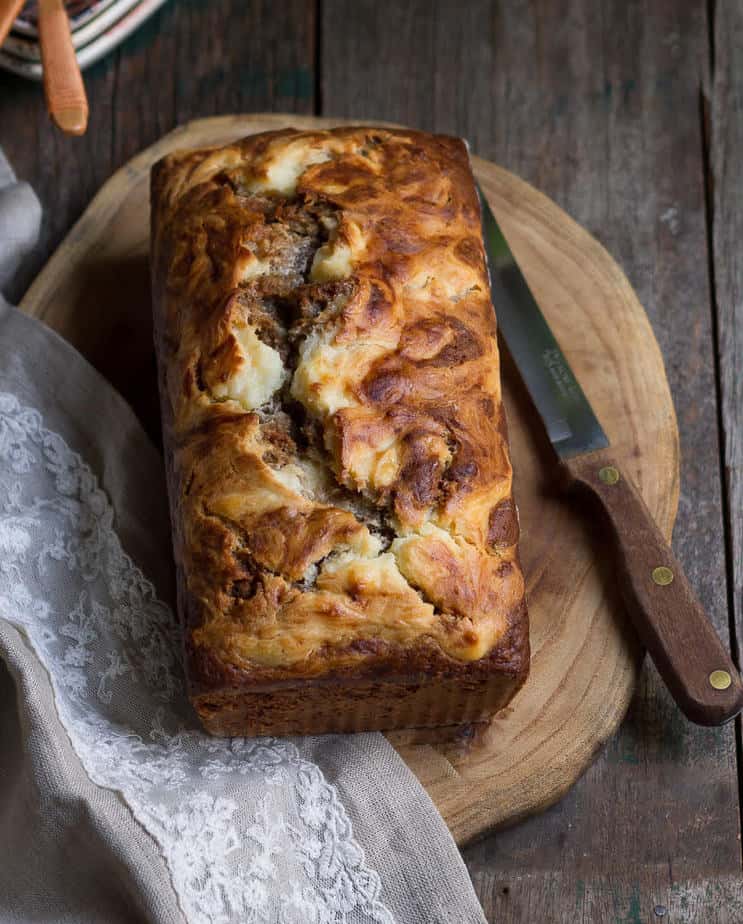 Banana bread with cream cheese on a wooden board with a knife.
