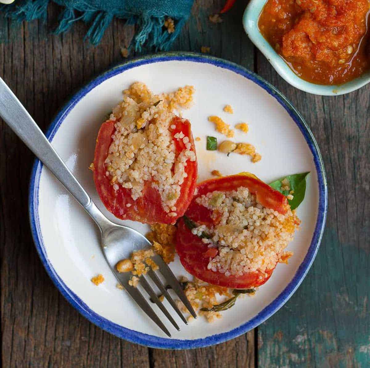 A stuffed tomato on a plate cut in half with a fork.