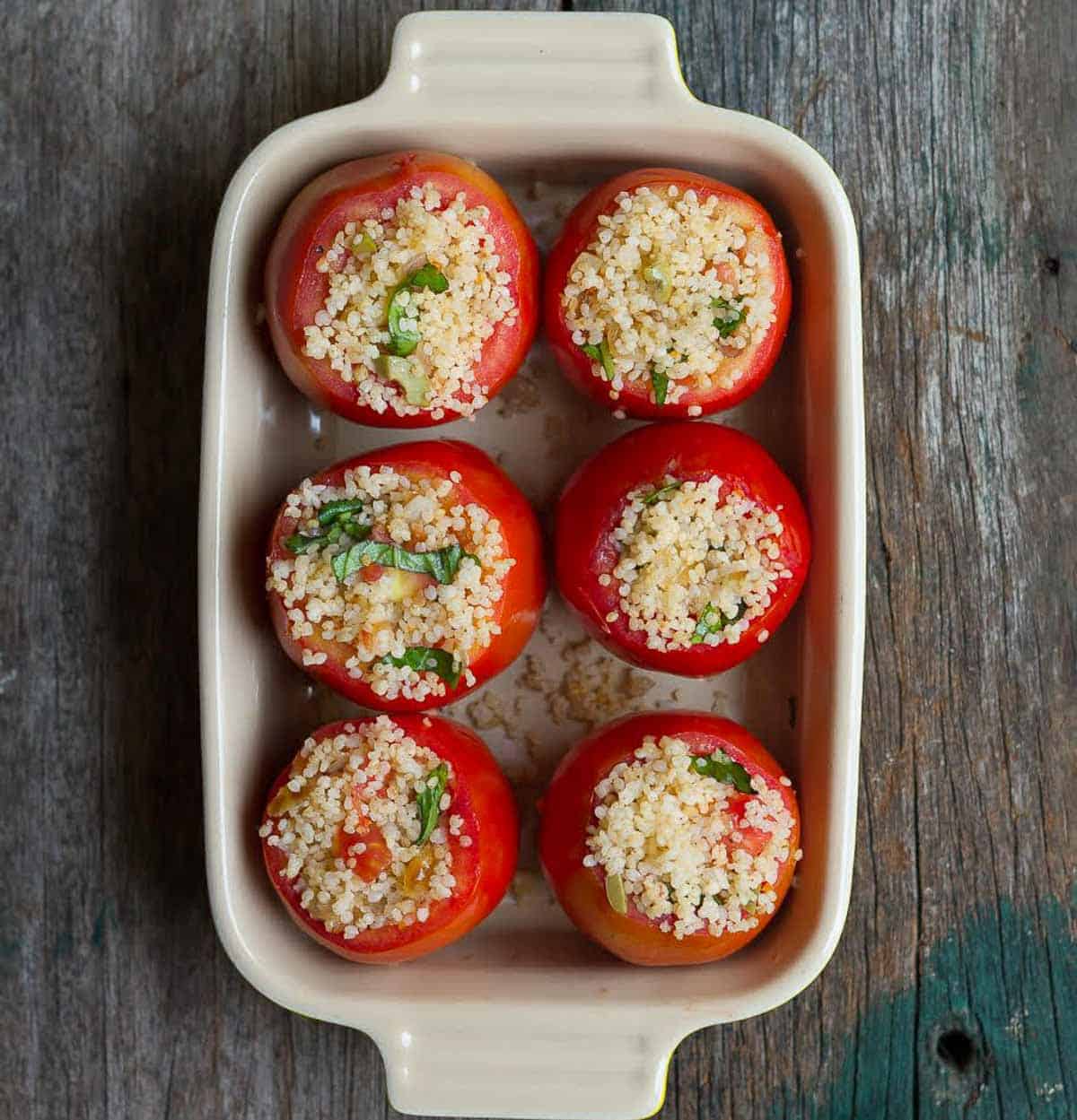 6 tomatoes stuffed with millet mixture in a baking dish.