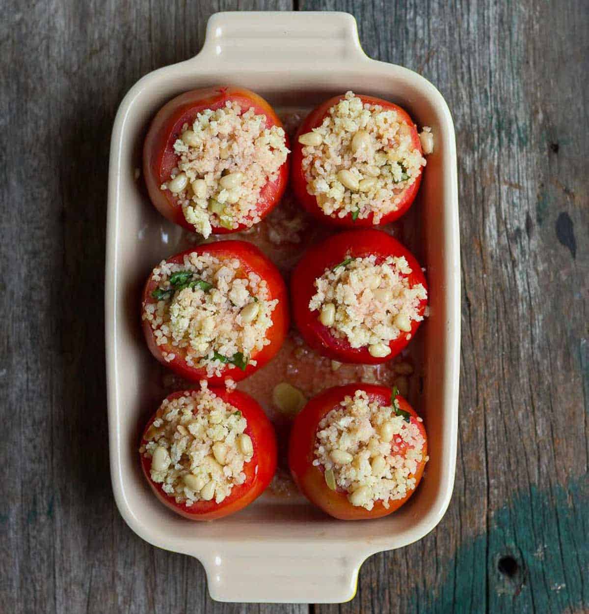 Stuffed tomatoes topped with panko and pinenuts in a baking dish.