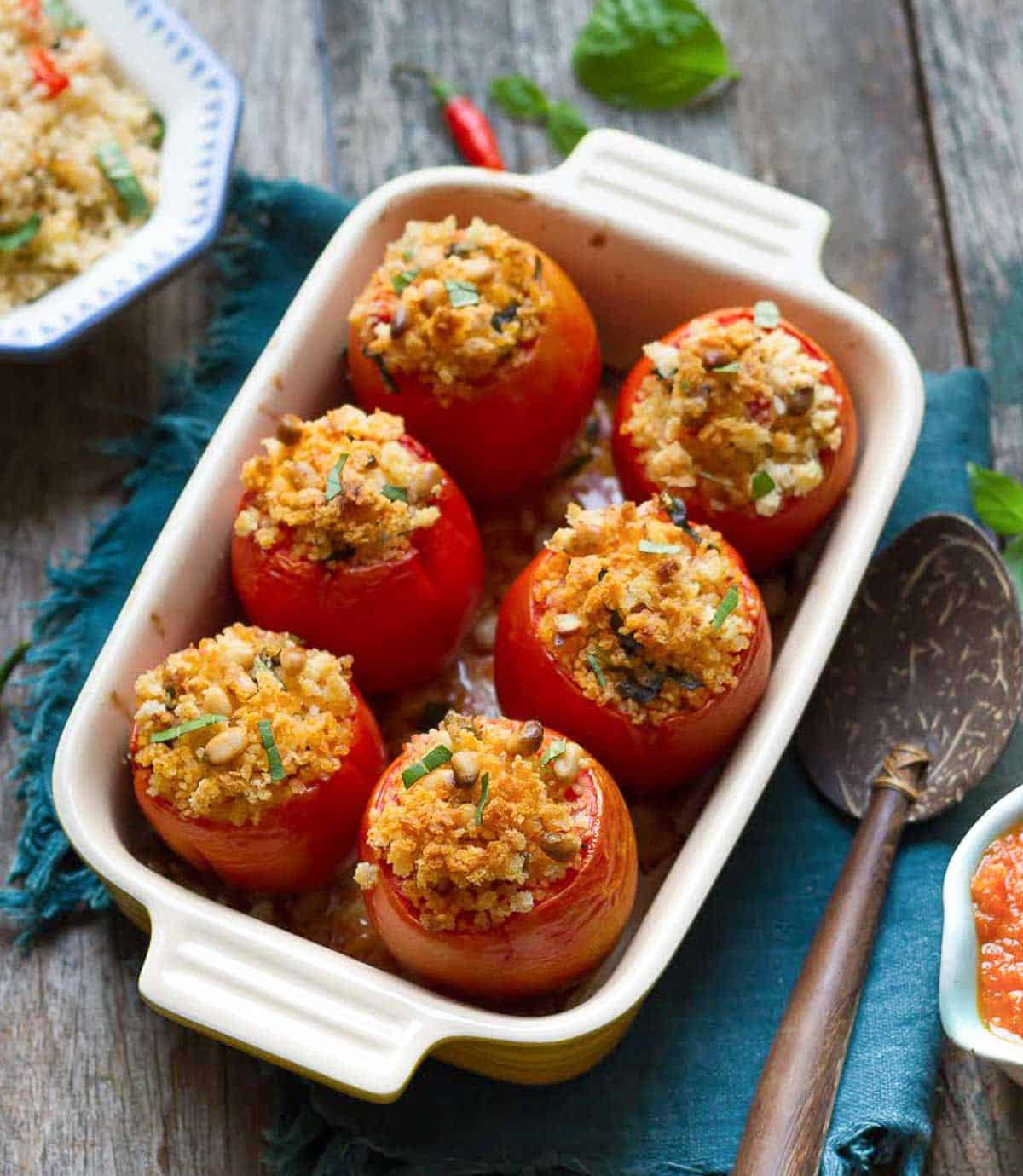 Baked stuffed tomatoes in a baking dish with ingredients around.