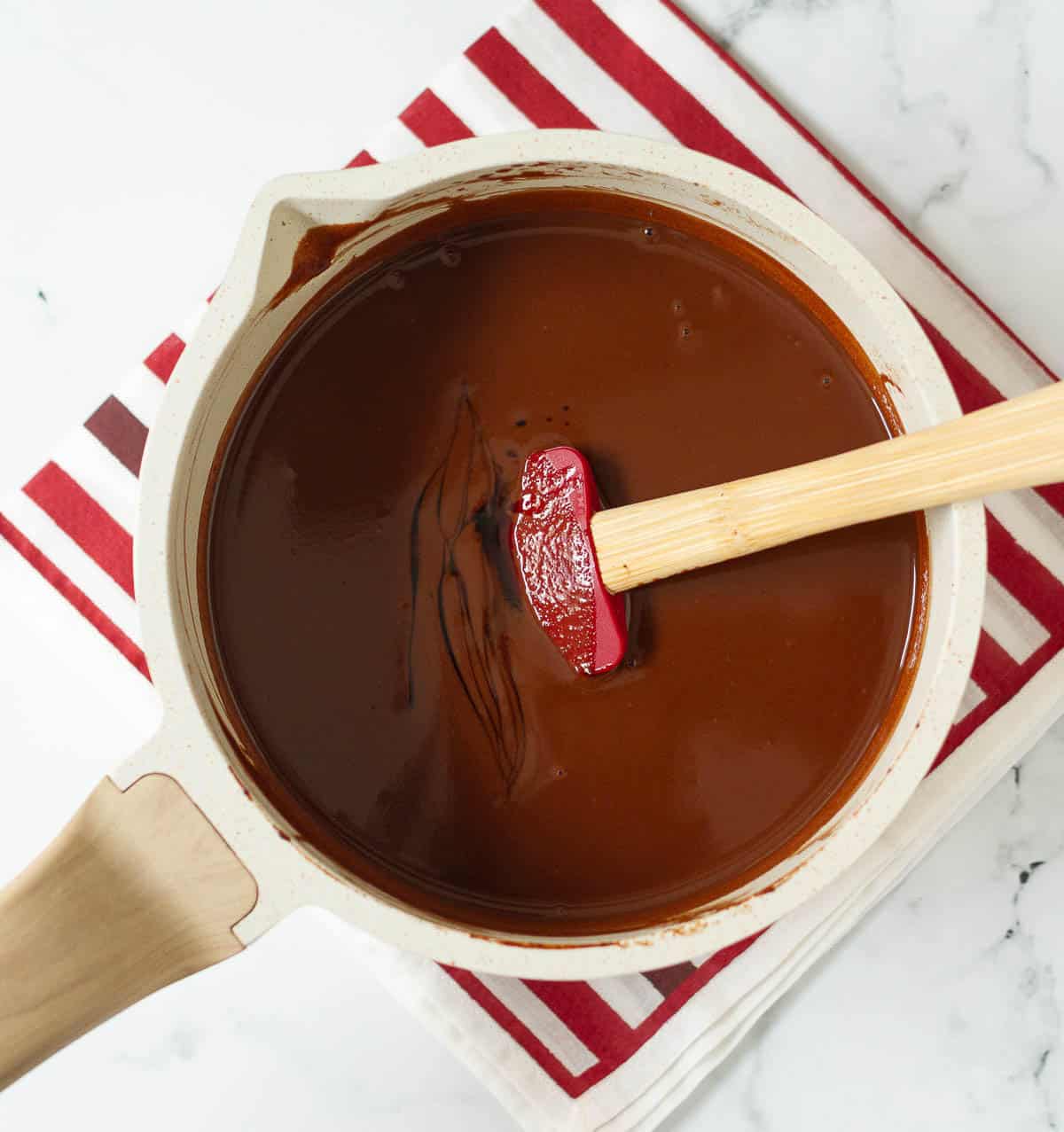 Vanilla extract on top of chocolate mixture in a saucepan with a red spatula.