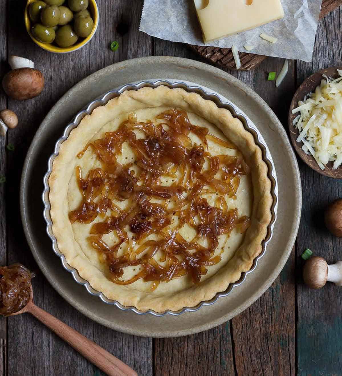 baked pie crust topped with caramelized onions and ingredients in the background.