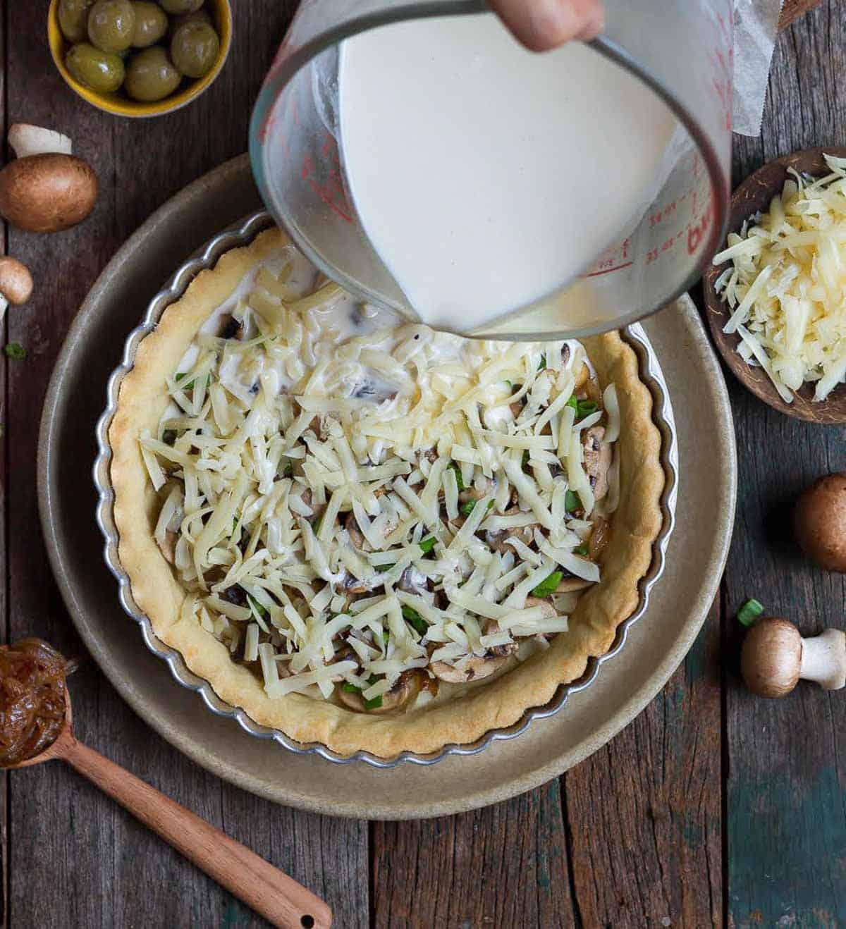 pouring custard into the pie crust with mushrooms, cheese and caramelized onions.
