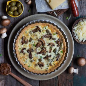 mushroom quiche on a platter with ingredients in the background.