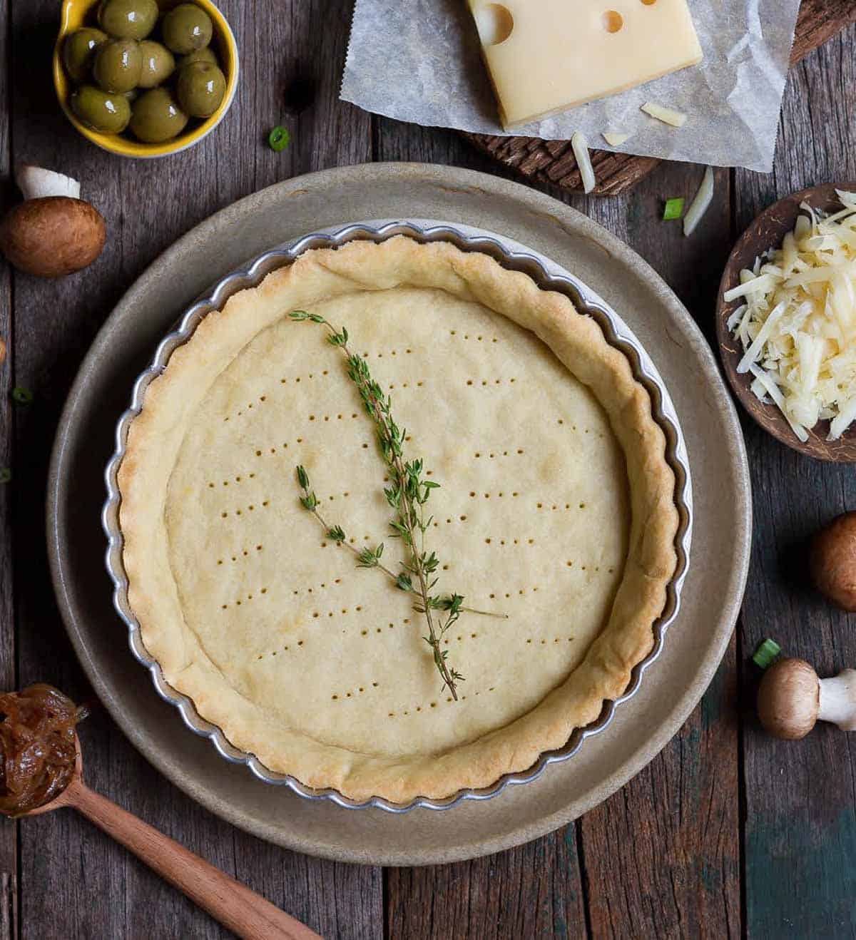 pie crust in a pie pan with a sprig of thyme and ingredients in the background.