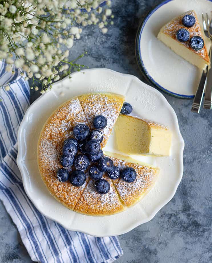 Japanese cheesecake topped with blueberries on a plate with one slice kept sideways.