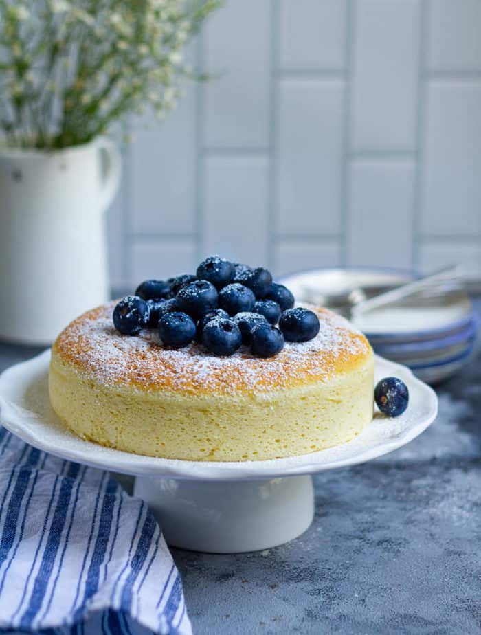 Cheesecake on a cakestand with blueberries and powdered sugar on top.
