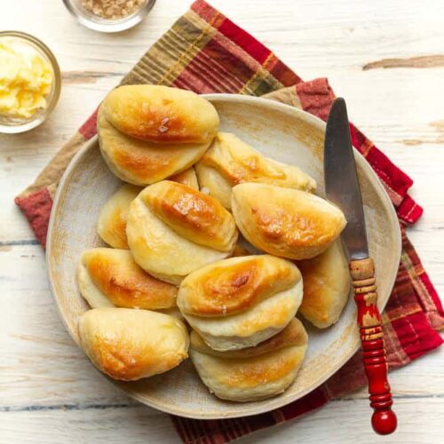 Parker House Rolls on a plate with a butter knife and butter.