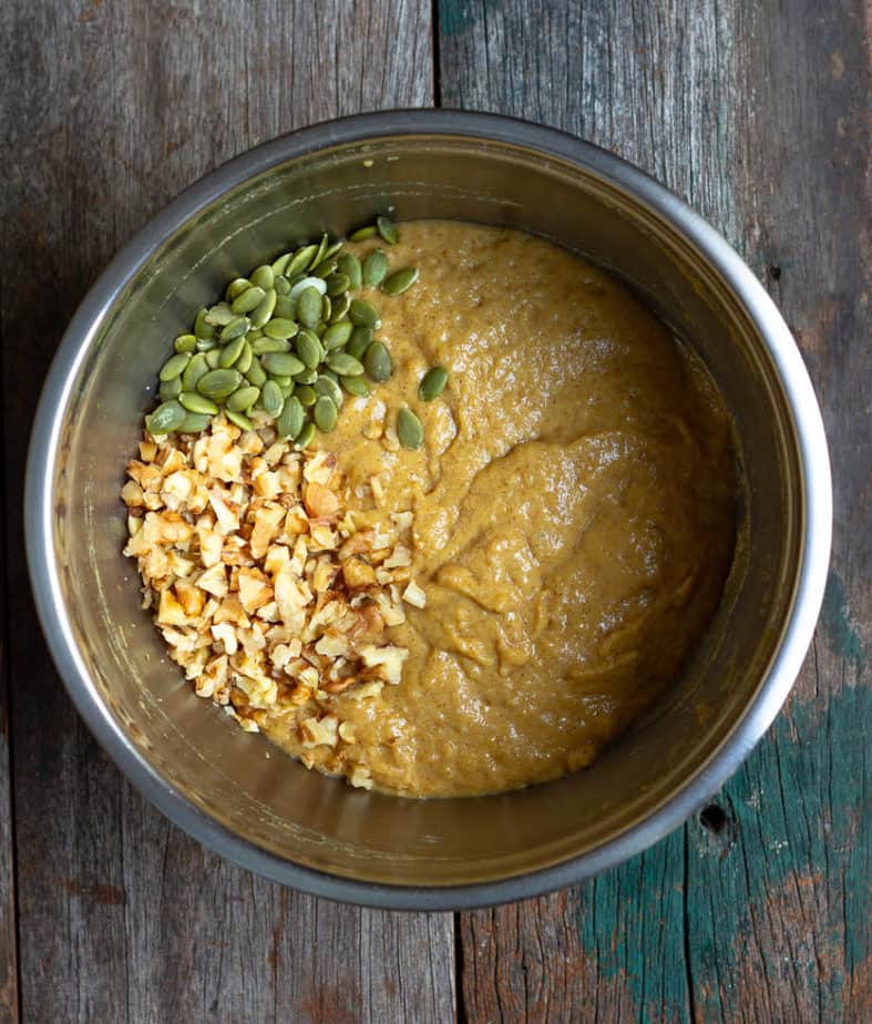 pumpkin seeds and walnuts on top of bread batter in a mixing bowl.