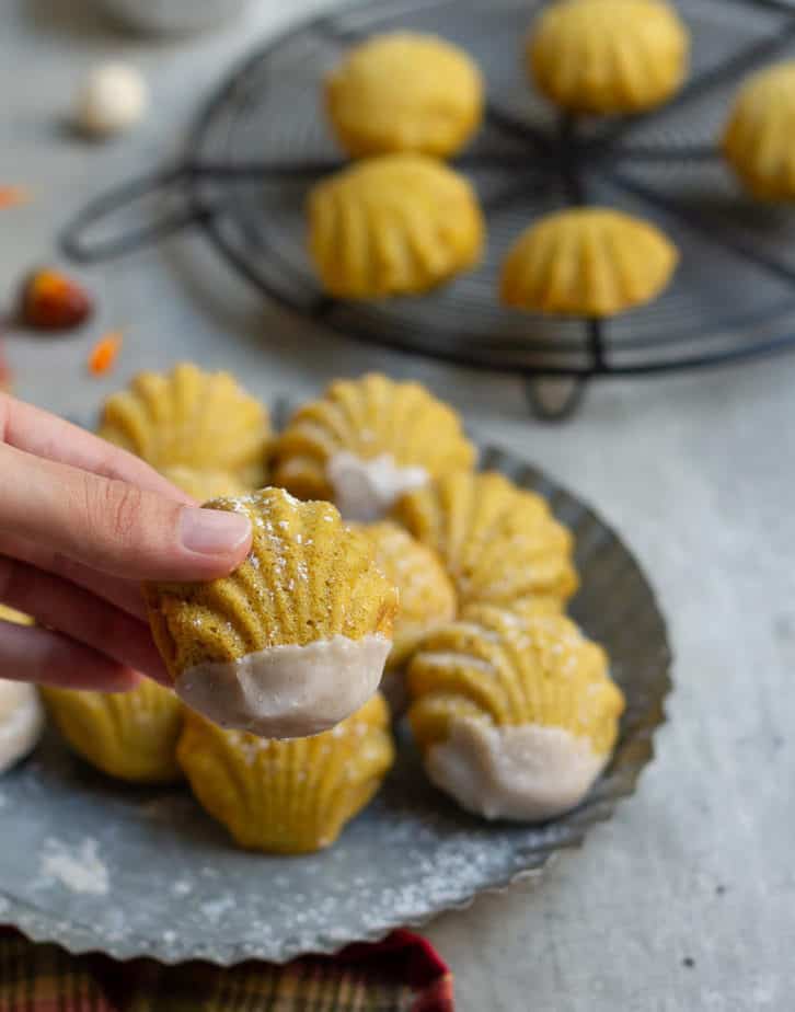 a hand holding a madeleine dipped in pumpkin pie spice glaze.