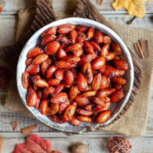 A bowl of roasted almonds on a wooden board with ingredients around.