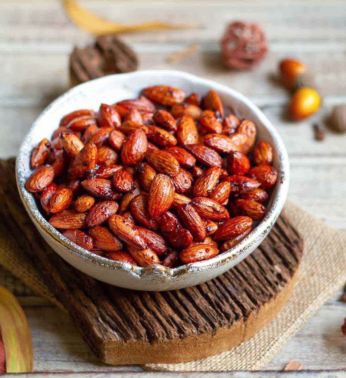 Roasted almonds in a bowl on a wooden board with fall decor around.