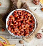 A bowl of roasted almonds on a wooden board with ingredients around.