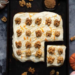 Pumpkin sheet cake with cream cheese frosting and walnuts on a black tray.