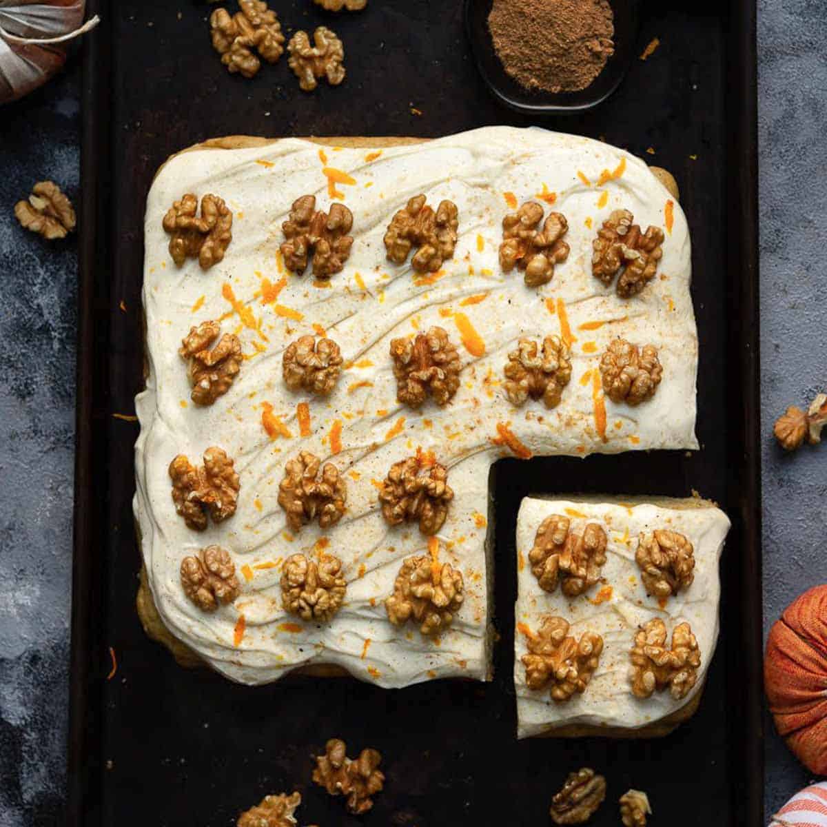 Pumpkin sheet cake with cream cheese frosting and walnuts on a black tray.