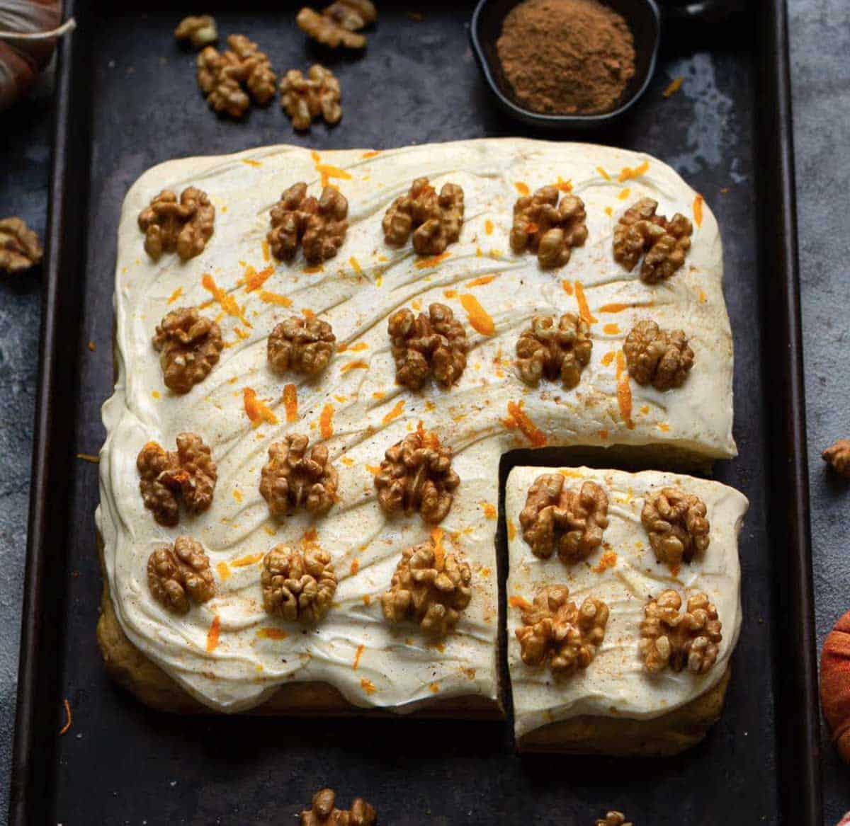 A pumpkin cake with frosting and walnuts on a black tray.