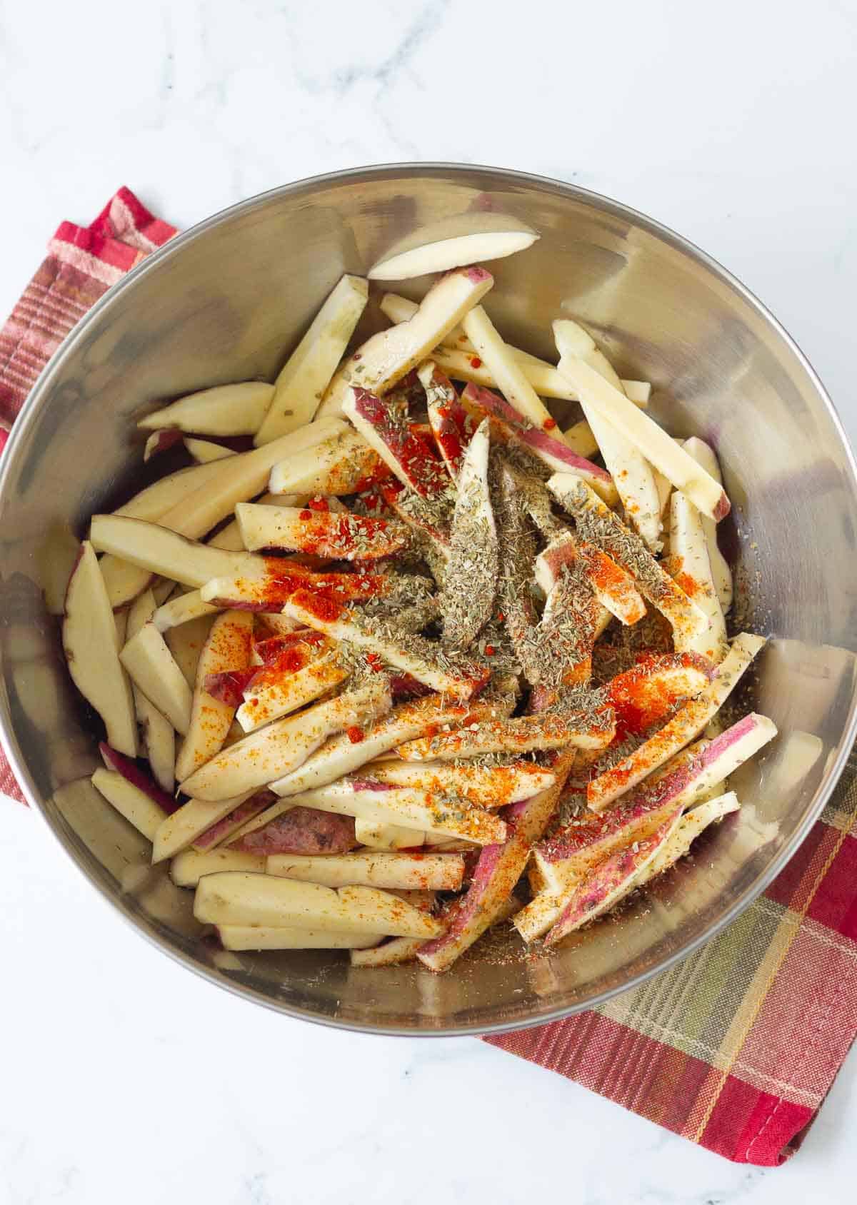 Sliced sweet potatoes with spices in a mixing bowl.