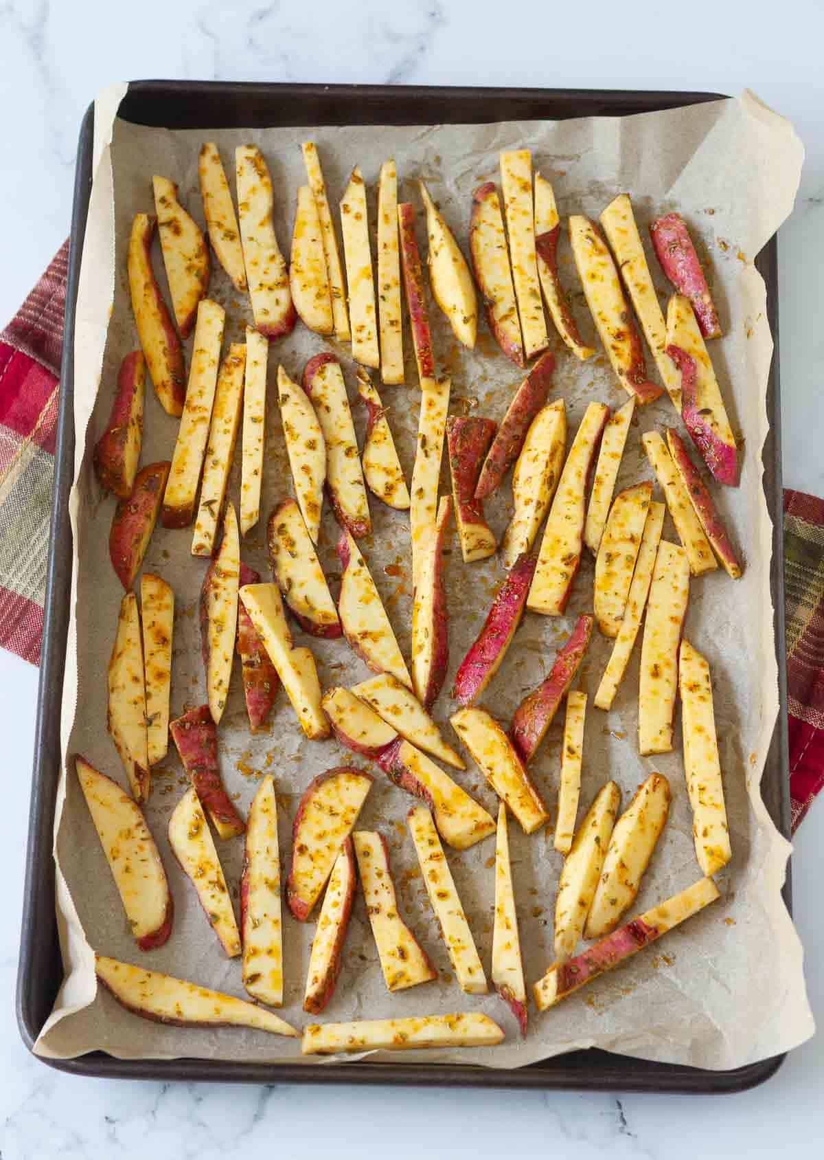 Sliced sweet potato on a parchment-lined baking tray.