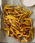 Baked sweet potato fries on parchment paper with a dip.