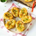 Loaded cheesy baked potatoes on a plate on a kitchen towel.