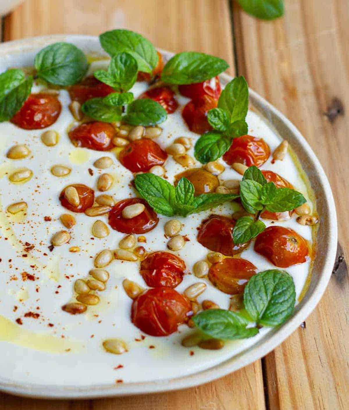 A bowl of dip garnished with pinenuts, tomatoes, and mint.
