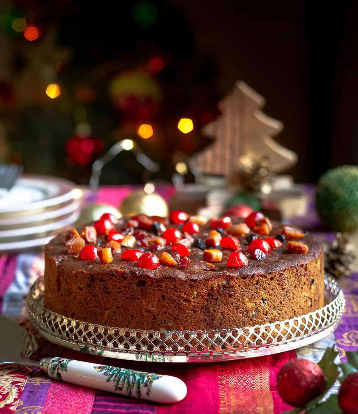 christmas cake on a serving platter with christmas decorations around.