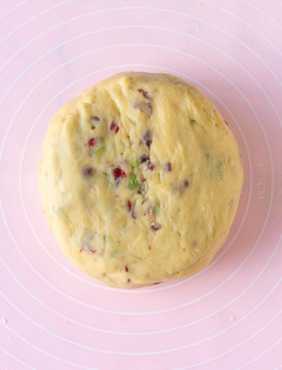 biscotti dough ball with cranberries and pistachios on a pink silicone mat.