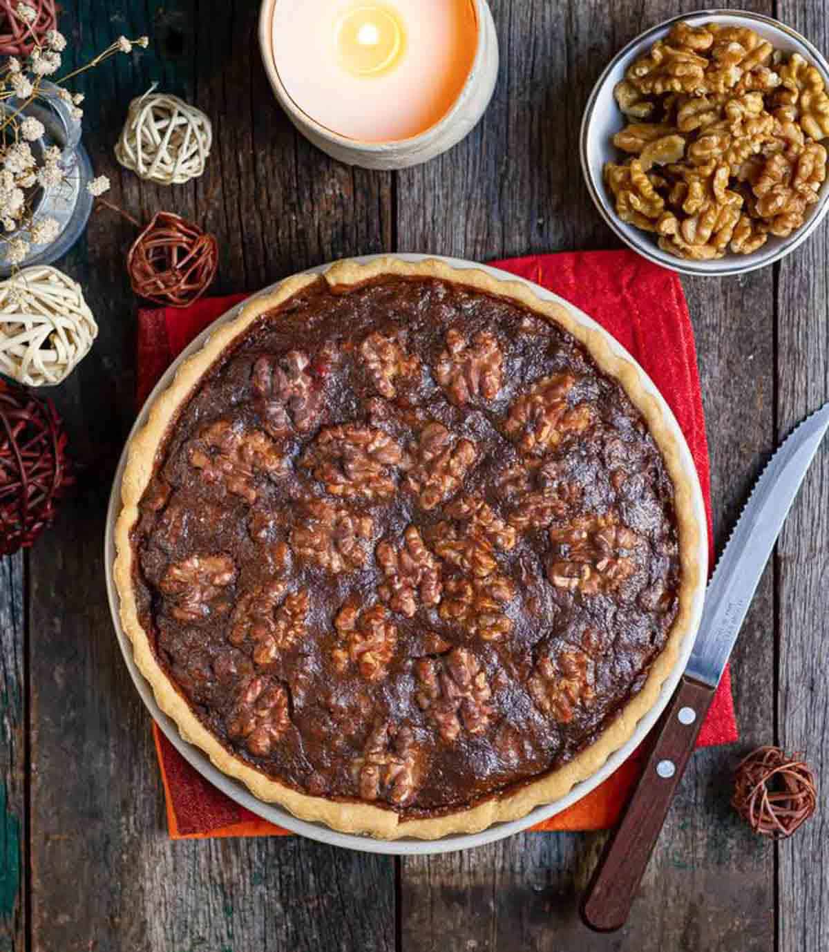 walnut pie with a knife on a red napkin surrounded by ingredients and props.