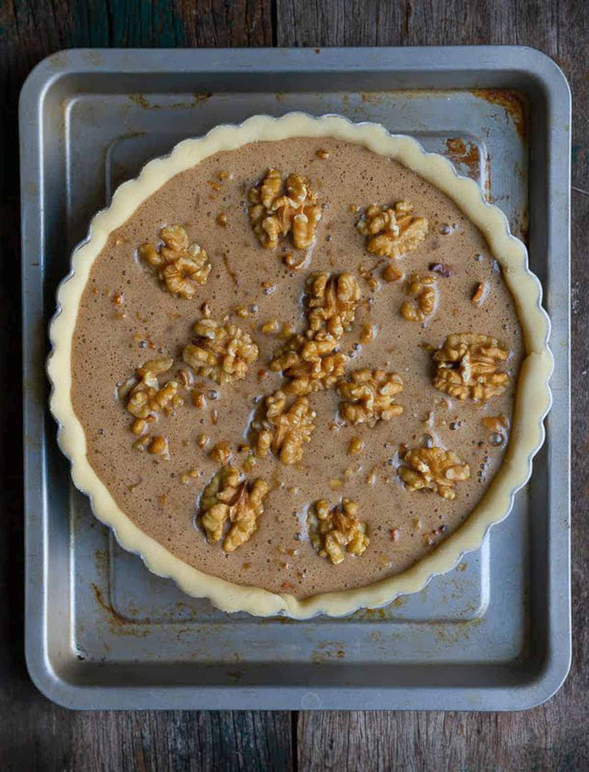 unbaked walnut pie in a pie dish on a tray.