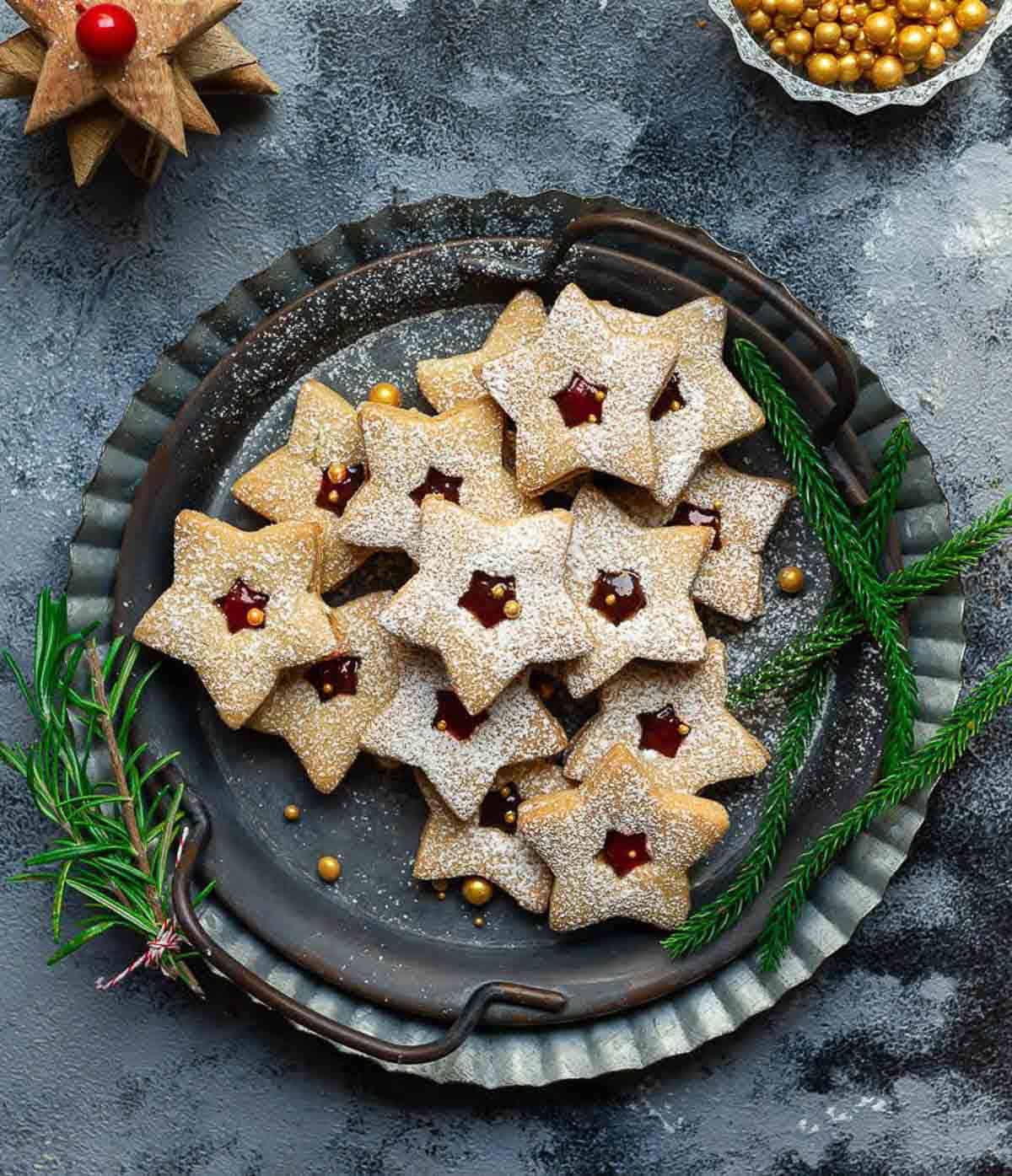 linzer cookies on a metal serving tray with green Christmas decorations.