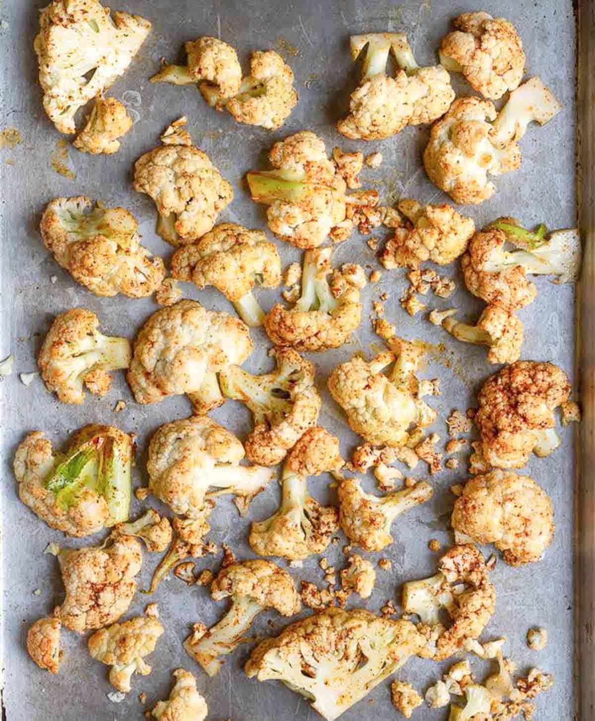 cauliflower florets tossed with olive oil and seasoning on a baking tray.