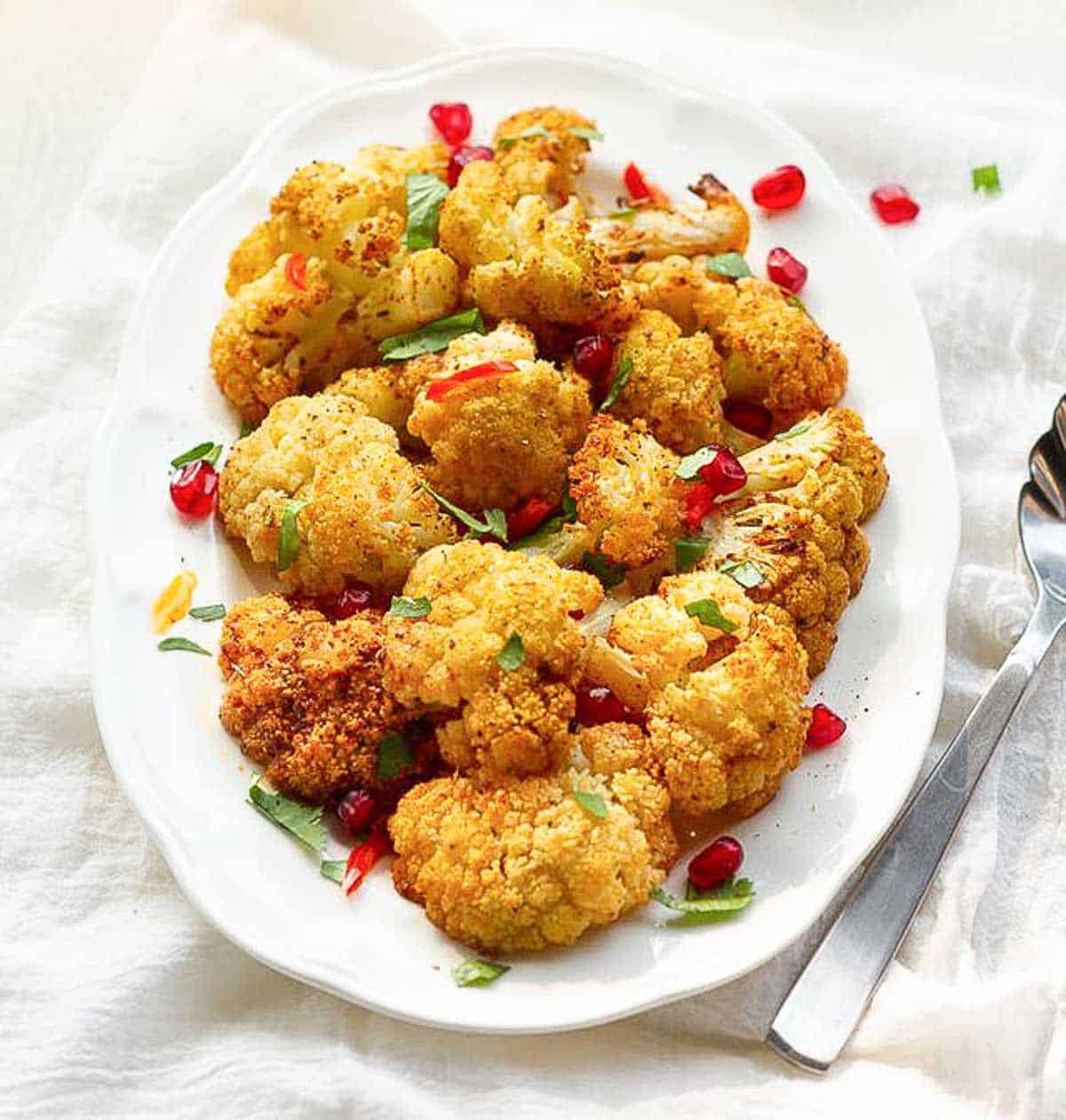 roasted cauliflower on a platter garnished with cilantro, pomegranates and red chilies.