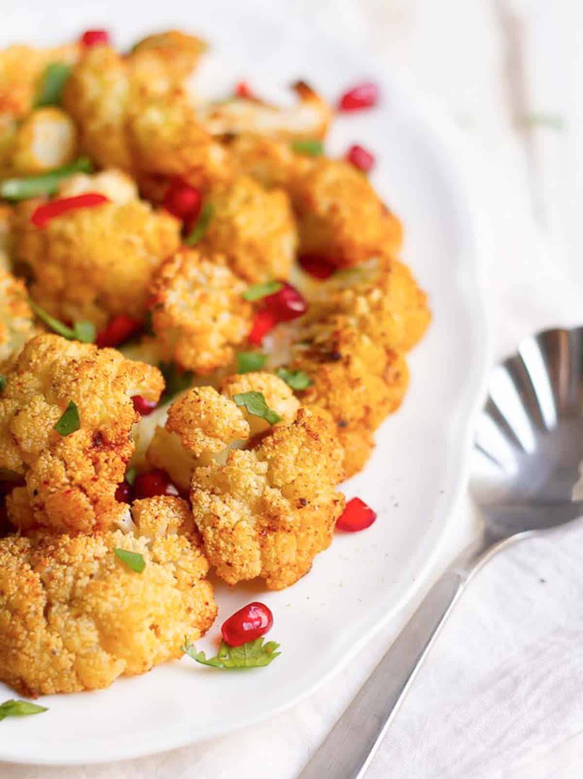 roasted cauliflower on a serving dish with pomegranate, red chilies and cilantro on top.
