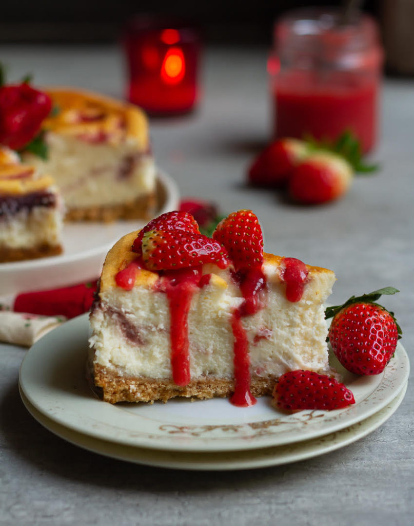 A slice of strawberry swirl cheesecake on a plate topped with strawberry sauce.