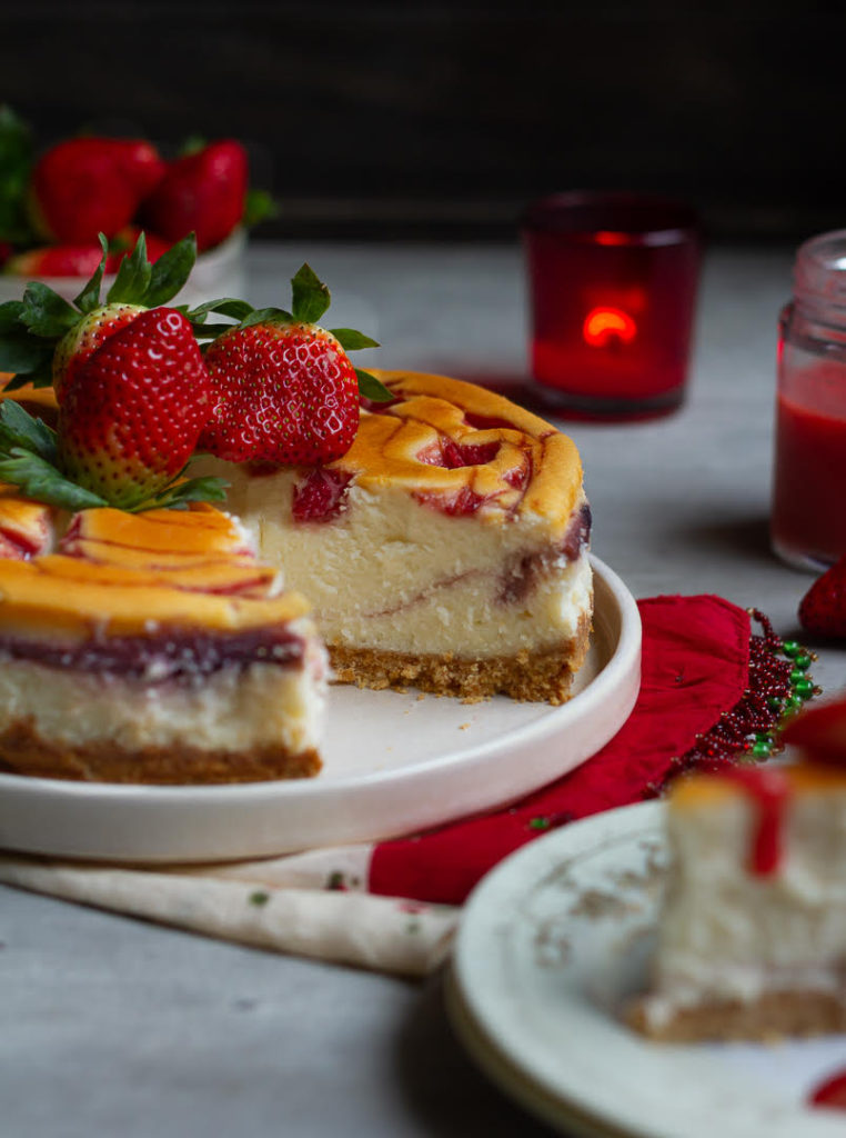 Strawberry cheesecake on a platter with a slice taken out to show the texture.