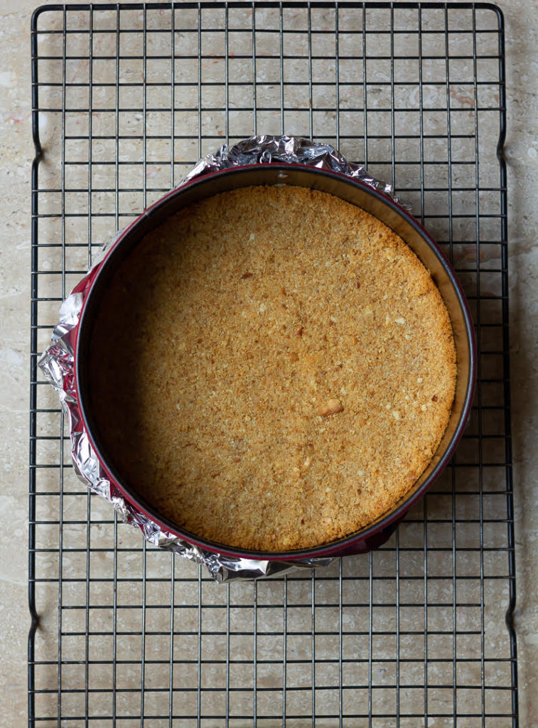 Baked crust for Strawberry cheesecake in a round cake pan on a cooling rack.