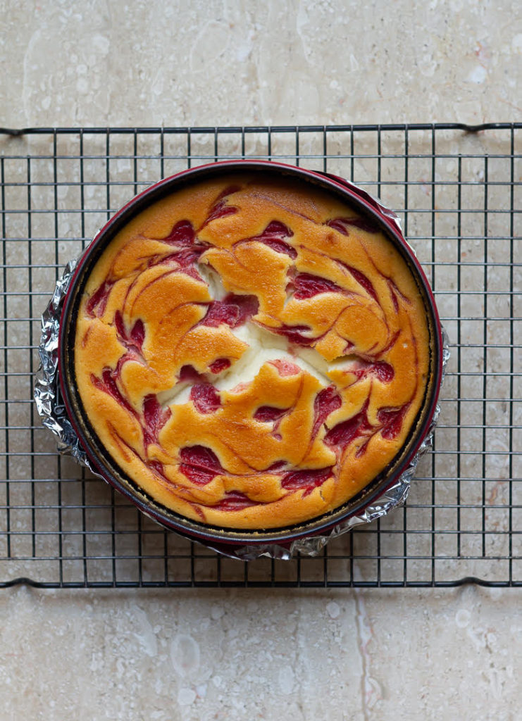 Baked strawberry cheesecake in a round cake pan on a cooling rack.