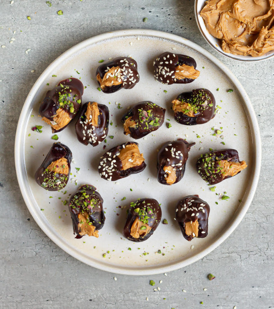 Stuffed dates dipped in chocolate and topped with pistachios and sesame seeds on a plate.