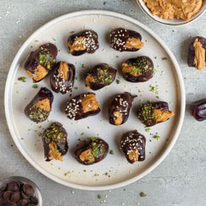 Peanut butter stuffed dates dipped in chocolate and topped with pistachios on a plate.