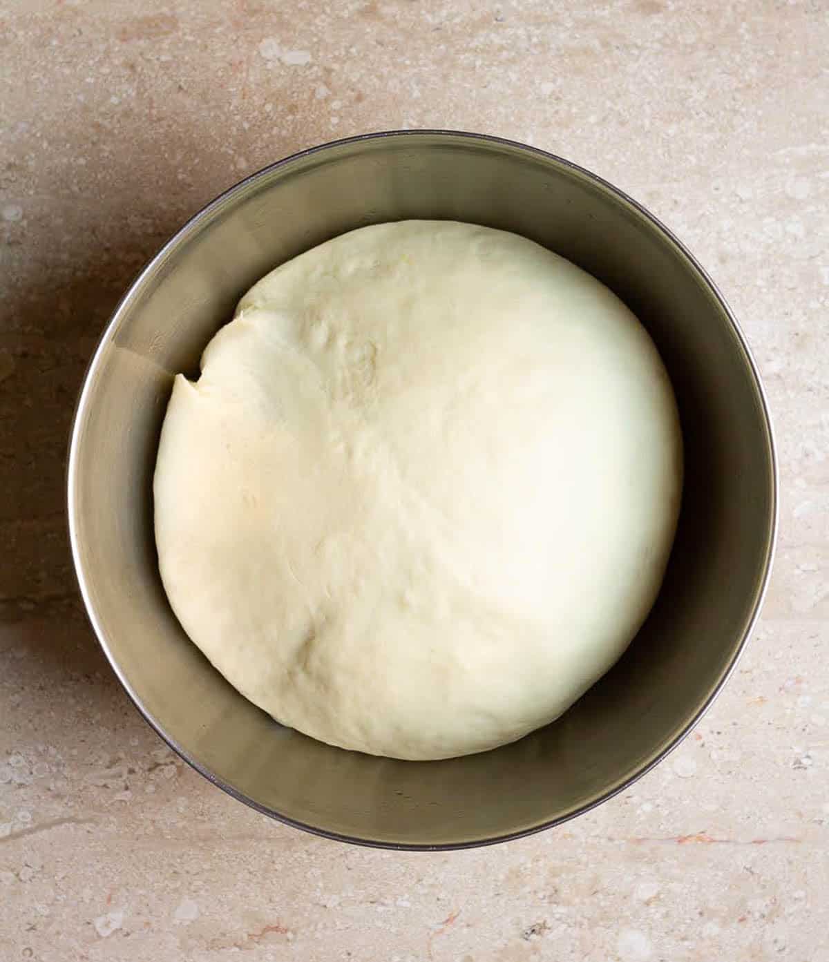 Proofed bread dough in a stainless steel bowl.