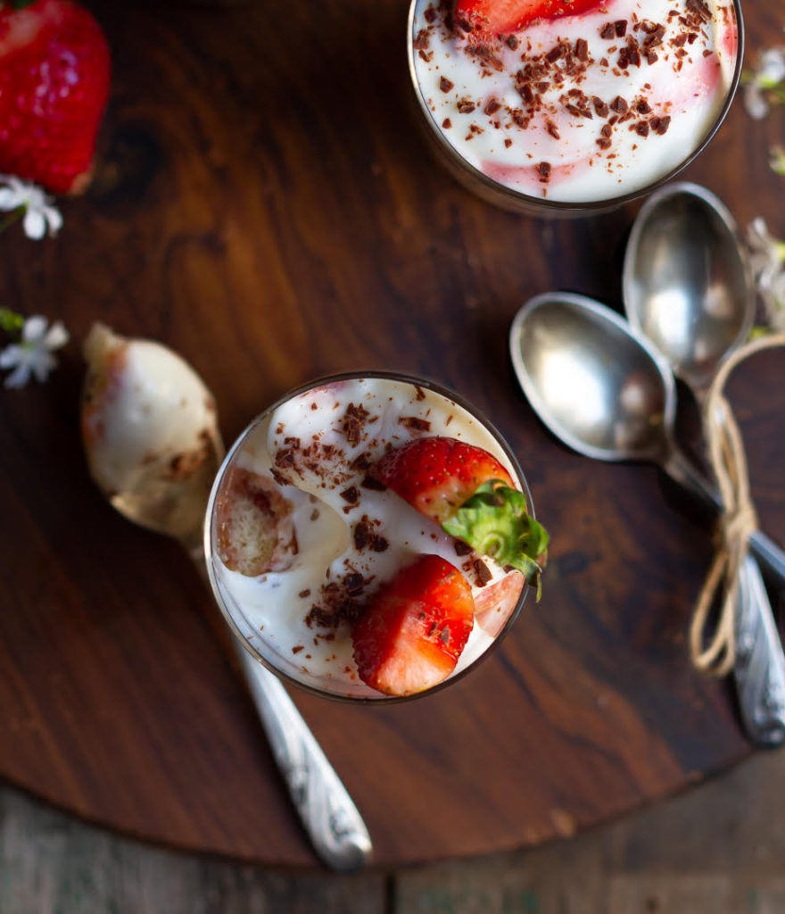 Strawberry tiramisu in a glass with a bite taken with a spoon on a wooden board.