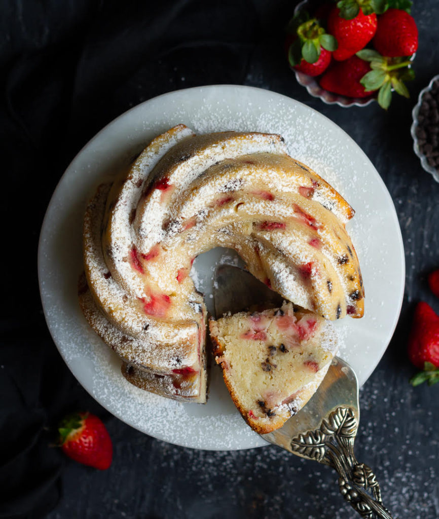 strawberry cake on a cake stand with one slice on a cake server to show the texture.