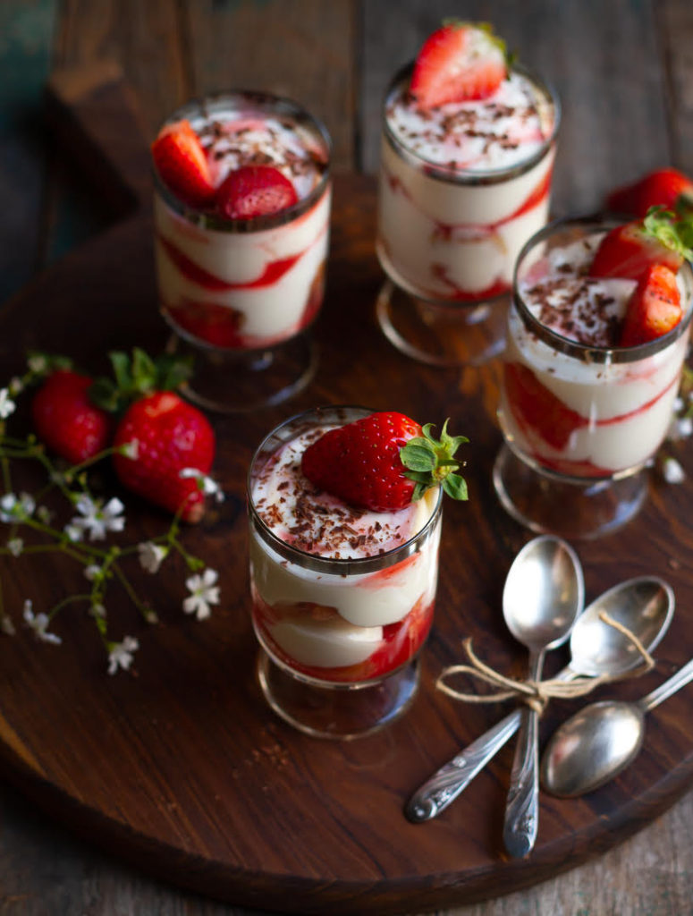 tiramisu in 4 dessert glasses topped with fresh strawberries and chocolate shavings.