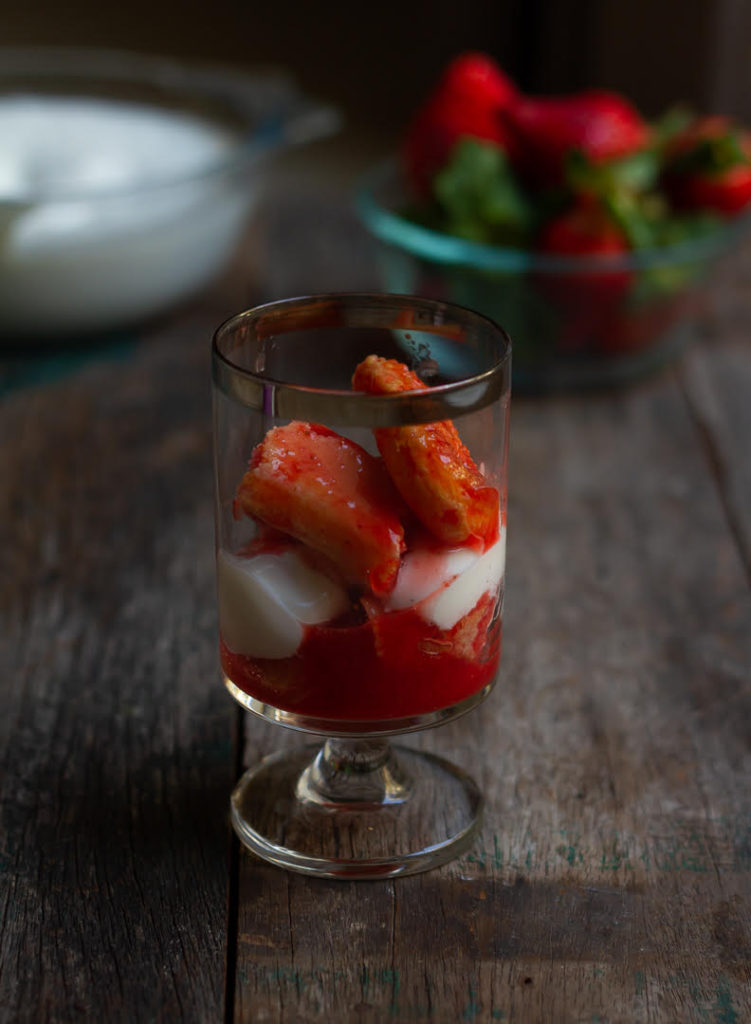 layers of strawberry soaked ladyfinger cookies with mascarpone cheese in a dessert glass.